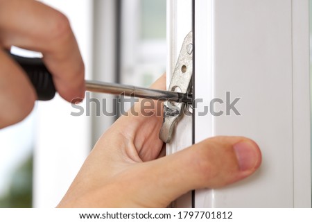 handyman adjusting white pvc plastic window indoors. worker using screwdriver to repair upvc window. homework maintenance. Royalty-Free Stock Photo #1797701812