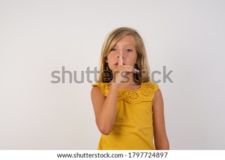 Little girl with beautiful blonde hair over white background  asking to be quiet with finger on lips. Silence and secret concept.