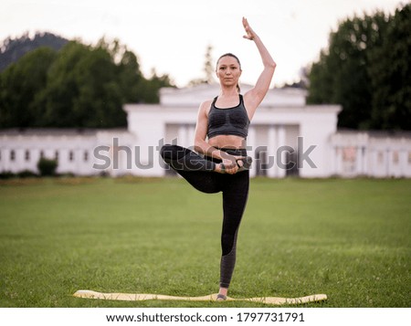 Beautiful young woman lying on a yellow mattress, pose while wearing a tight sports outfit in the park doing pilates or yoga, stretch exercises