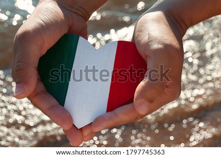 wooden heart painted in the colors of the flag of Italy green, white and red lies in men's palms against background of sea in blur