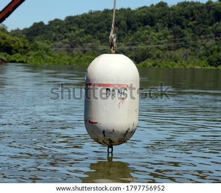 A worn and weathered river dam warning buoy hanging over the water and whose printed message has faded to just state dang