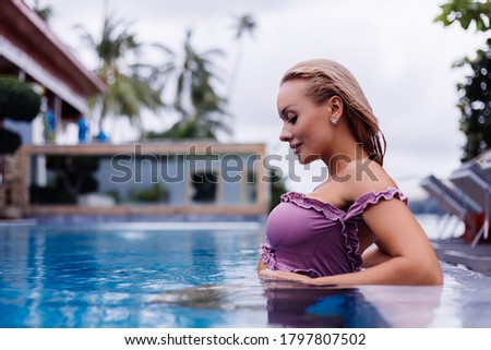 Fashion portrait of caucasian woman in bikini in blue swimming pool on vacation at coudy day, natural light.