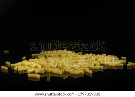 Uncooked macaroni on black background and reflective base.