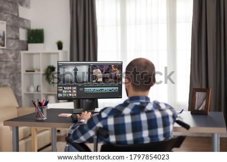 Professional video editor in wheelchair because of walking disability. Young invalid film maker doing his business online, using high technology, sitting in his apartment, working remotely in special