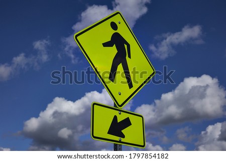 Pedestrian crossing sign against blue sky. A yellow warning sign that alerts road users to unexpected conditions ahead and reminds them that it is a place designated for pedestrians to cross a road.