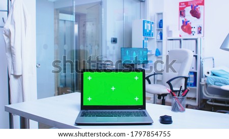 Footage of laptop with green screen display in hospital Doctor wearing coat arriving in health clinic and nurse working on computer in cabinet. Notebook with replaceable screen in medic clinic.