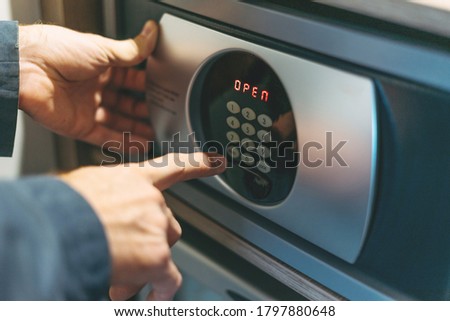 Adult man in blue jacket uses safe in hotel room Royalty-Free Stock Photo #1797880648