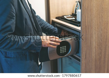 Adult man in blue jacket uses safe in the hotel room Royalty-Free Stock Photo #1797880657