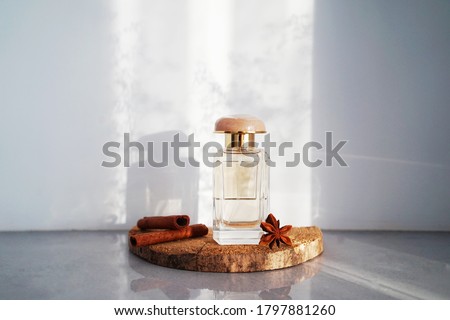  
glass perfume bottle with fragments of wood bark, cinnamon sticks and anise stars with racy delicate shadows in the background. The concept of a spicy, woody scent.                               Royalty-Free Stock Photo #1797881260