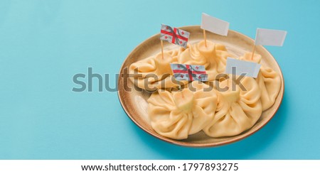 Khinkali cooked on a ceramic plate served over pastel blue background. Copy space banner. Delicious meat dumplings. Traditional Georgian cuisine. Georgian flag picture.