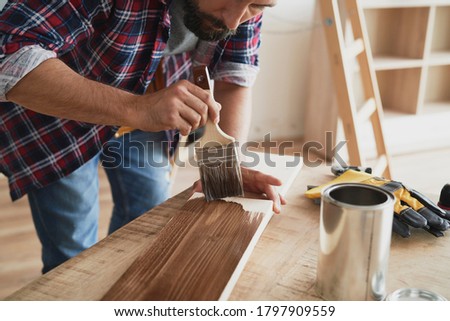 Man painting a raw board with a protective preparation                                Royalty-Free Stock Photo #1797909559