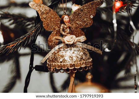 Close up picture of xmas decoration on the tree. Ball with fairy in gold color shade and pine tree on the background, as decor elect for Christmas tree. Greeting card for winter holidays.