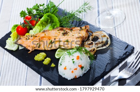 Picture of  tasty  fried trout  fillet with rice, tomatoes and greens on black plate