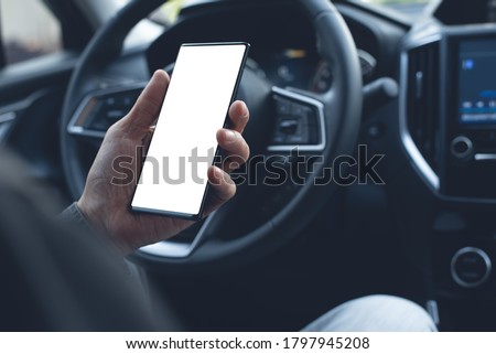 Mock up image of man driver hand using blank white screen mobile smart phone inside a car, searching location via gps navigator application, close up