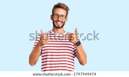 Handsome blond man with beard wearing casual clothes and glasses success sign doing positive gesture with hand, thumbs up smiling and happy. cheerful expression and winner gesture. 