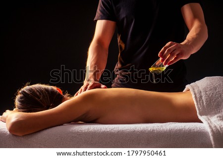 young indian woman lying on the table and getting ayurvedic massage with organic oil or honeyed in dark room.massagist male pouring out client back Royalty-Free Stock Photo #1797950461