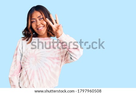 Young beautiful mixed race woman wearing casual tie dye sweatshirt showing and pointing up with fingers number three while smiling confident and happy. 