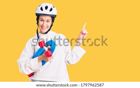 Beautiful brunette young woman wearing safety helmet and skate surprised with an idea or question pointing finger with happy face, number one 