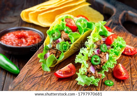Taco shells with lettuce, ground beef meat,  mashed avocado, tomato, red onion and jalapeno pepper, horizontal, on a wooden board, closeup