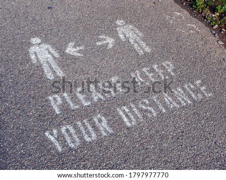 Painted 'please keep your distance' sign on pavement on crowded beach in tourist hotspot in Devon UK during COVID-19 pandemic