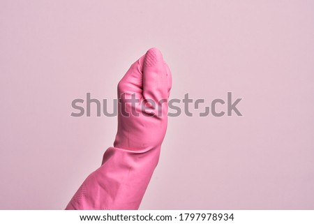 Hand of caucasian young man with cleaning glove over isolated pink background holding blank space with thumb finger, business and advertising