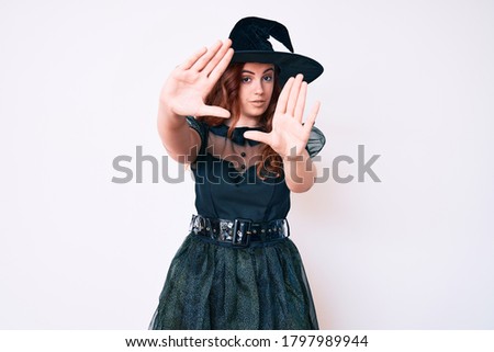 Young beautiful woman wearing witch halloween costume doing frame using hands palms and fingers, camera perspective 