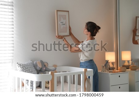 Decorator hanging picture on wall in baby room. Interior design
