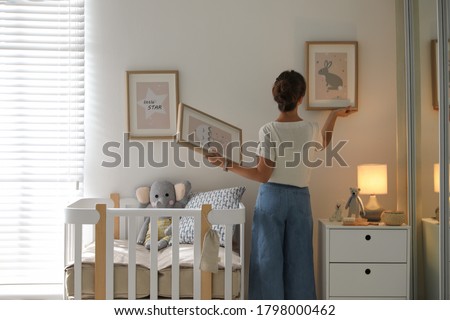 Decorator hanging pictures on wall in baby room. Interior design