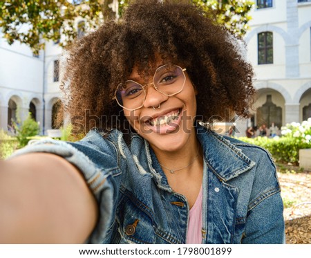 Beautiful young black Afro woman taking selfie with her smartphone in the park. Smiling at the camera of the phone to do a self portrait. Concept about lifestyle, technology and people. 