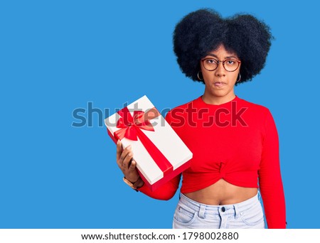 Young african american girl holding gift skeptic and nervous, frowning upset because of problem. negative person. 