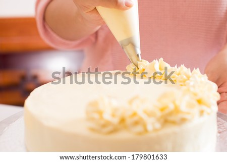 Close shot of a human hand frosting a cake with whipped cream on the foreground 