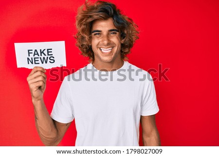 Young hispanic man holding fake news banner looking positive and happy standing and smiling with a confident smile showing teeth 