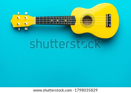 Yellow colored wooden ukulele guitar on the turquoise blue background. Overhead photo of ukulele with copy space. Royalty-Free Stock Photo #1798035829