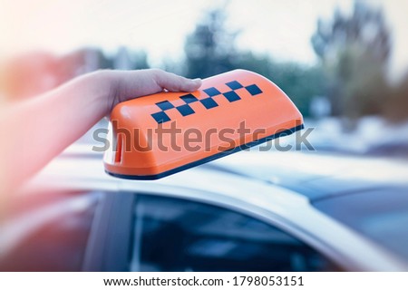 Orange sign of a taxi in the hands of a man on the background of a car. The driver went to work