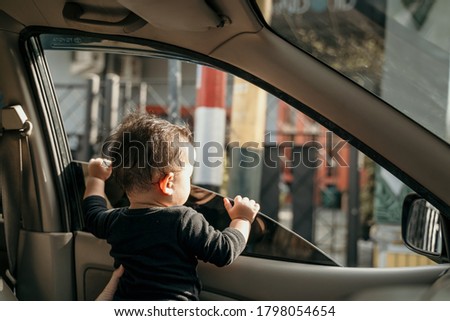 little baby in black stand in the car when the windows are opened while traveling by car