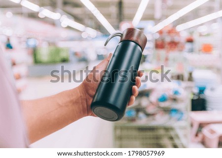 A man in a supermarket holds a thermos in his hands