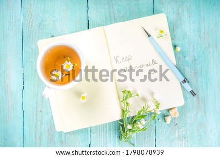 Chamomile tea mug with bouquet of Chamomile flowers of the valley and notes good morning, keep calm (calmomile) inscription, on turquoise wooden table, beautiful summer breakfast flat lay