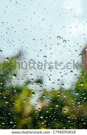 Rain drops on window pane glass surface with trees on the background.