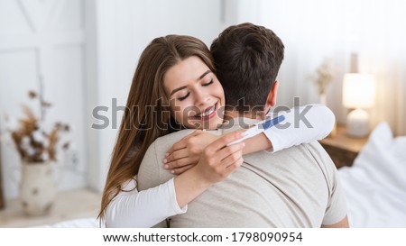 Expect a baby. Happy young woman hugging husband and looking at positive pregnancy test in interior of bedroom, panorama, free space Royalty-Free Stock Photo #1798090954