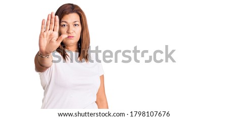 Middle age latin woman wearing casual white tshirt doing stop sing with palm of the hand. warning expression with negative and serious gesture on the face. 