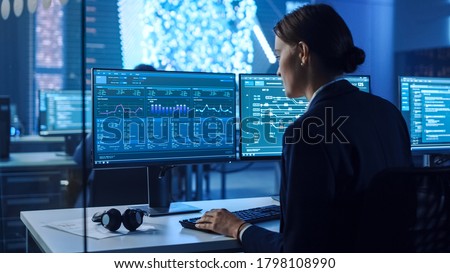 Confident Female Data Scientist Works on Personal Computer in Big Infrastructure Control and Monitoring Room with Neural Network. Woman Engineer in an Office Room with Colleagues. Royalty-Free Stock Photo #1798108990