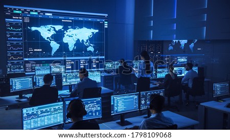 Team of Professional Computer Data Science Engineers Work on Desktops with Screens Showing Charts, Graphs, Infographics, Technical Neural Data and Statistics. Low Key Control and Monitoring Room. Royalty-Free Stock Photo #1798109068