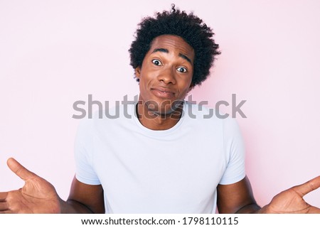 Handsome african american man with afro hair wearing casual clothes clueless and confused expression with arms and hands raised. doubt concept. 