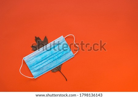 Medical disposable blue mask covers an oak leaf on the orange background, copy space.