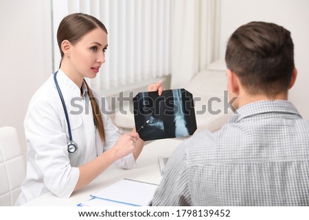 Orthopedist showing X-ray picture to patient at table in clinic
