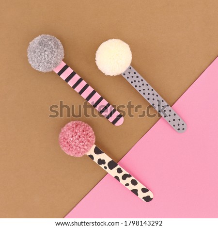 Handmade pompom book markers with painted ice creams sticks, top view hand crafted concept on brown and pink background