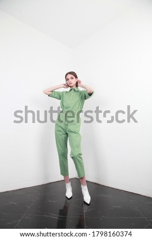 Full shot of a brown haired European lady with long hair in a summer cotton two piece suit, standing in a simple interior with white walls, studio photography, copy space