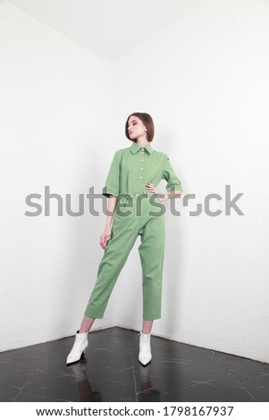 Full shot of a brown haired European lady with long hair in a summer cotton two piece suit, standing in a simple interior with white walls, studio photography, copy space