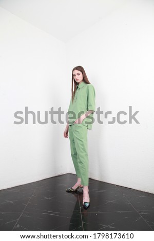 A romantic brown-haired lady in white leather boots is wearing figure-flattering jumpsuit and wide trouser legs. The light green cotton jumpsuit is perfect for every day and office work
