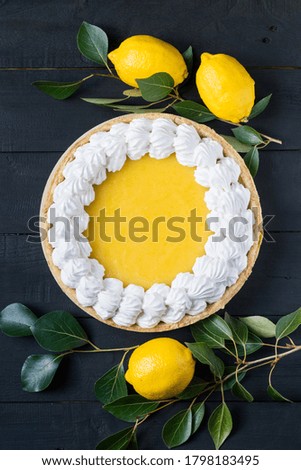 Homemade lemon pie with meringue with fresh lemons on black wooden background, top view.